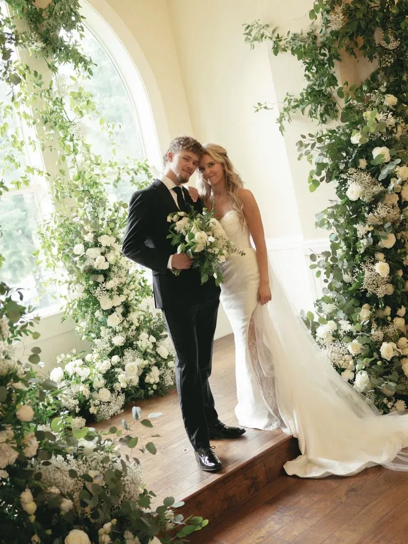 Couple standing in white florals beneath an arched window