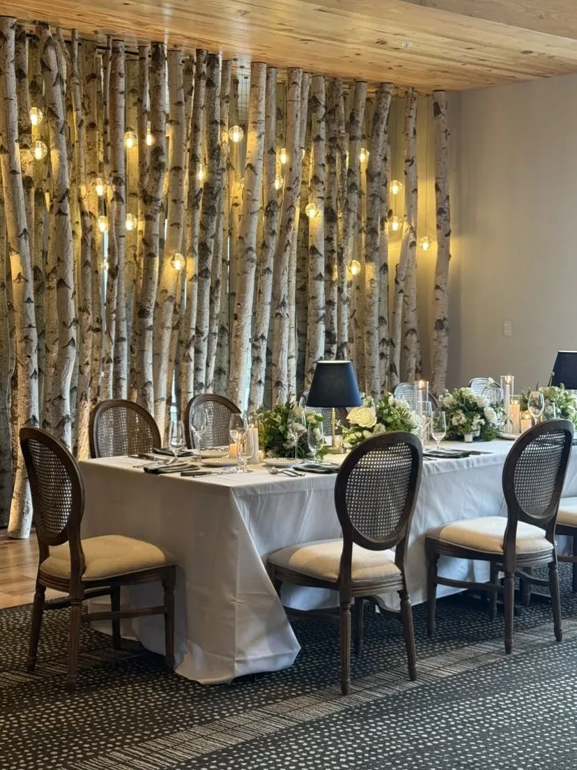 Indoor reception table with white roses set against a birch wall
