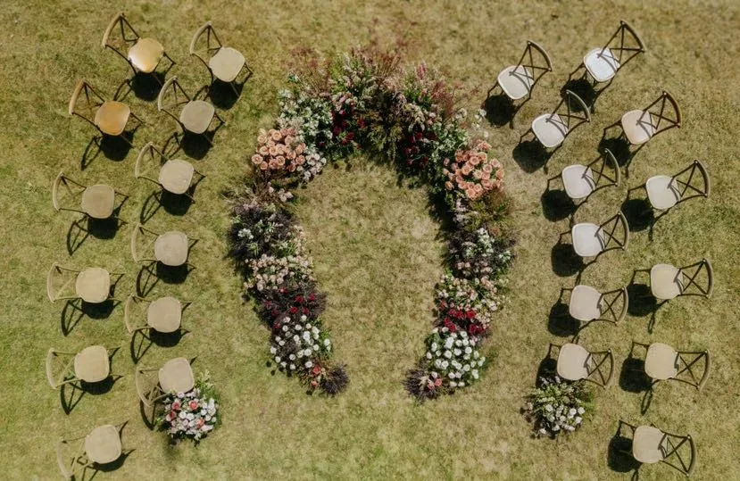 Overhead view of a U-shaped ground floral ceremony with wooden chairs on a lawn