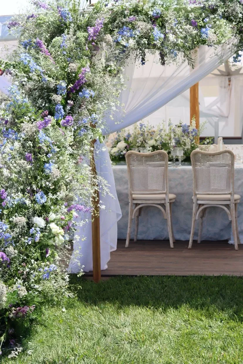 Blue and lavender floral column beside cane chairs and white tent draping