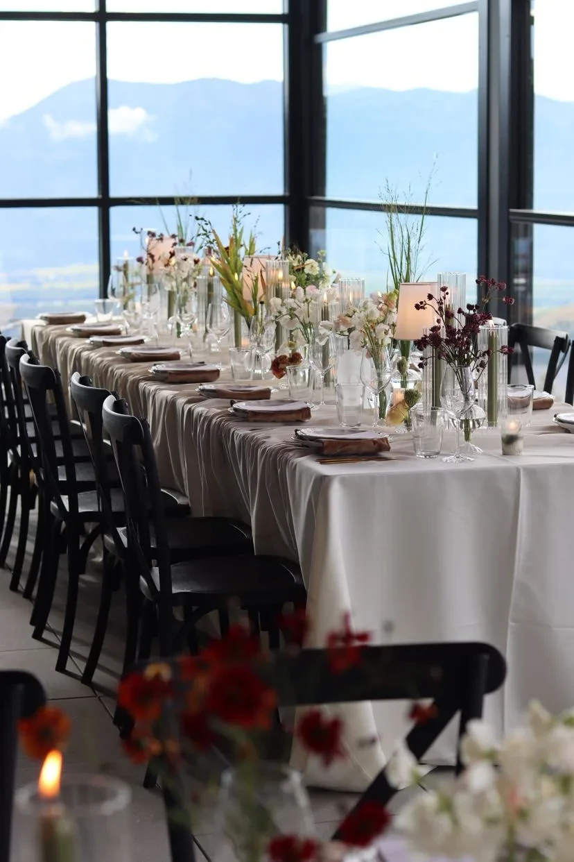 Long indoor table with tapers, grasses and mountain windows at the end of the room