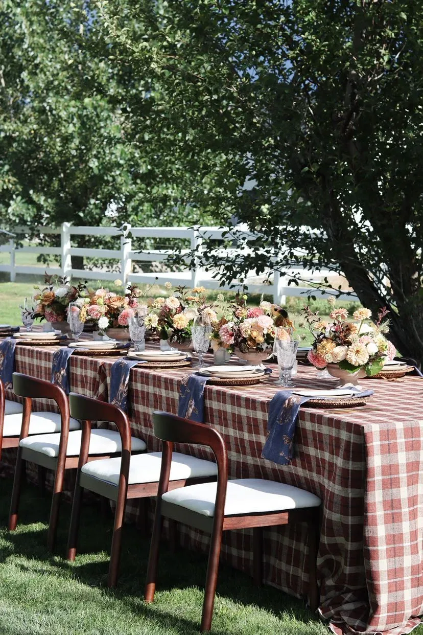 Outdoor table with red-brown plaid and peach bowls of flowers