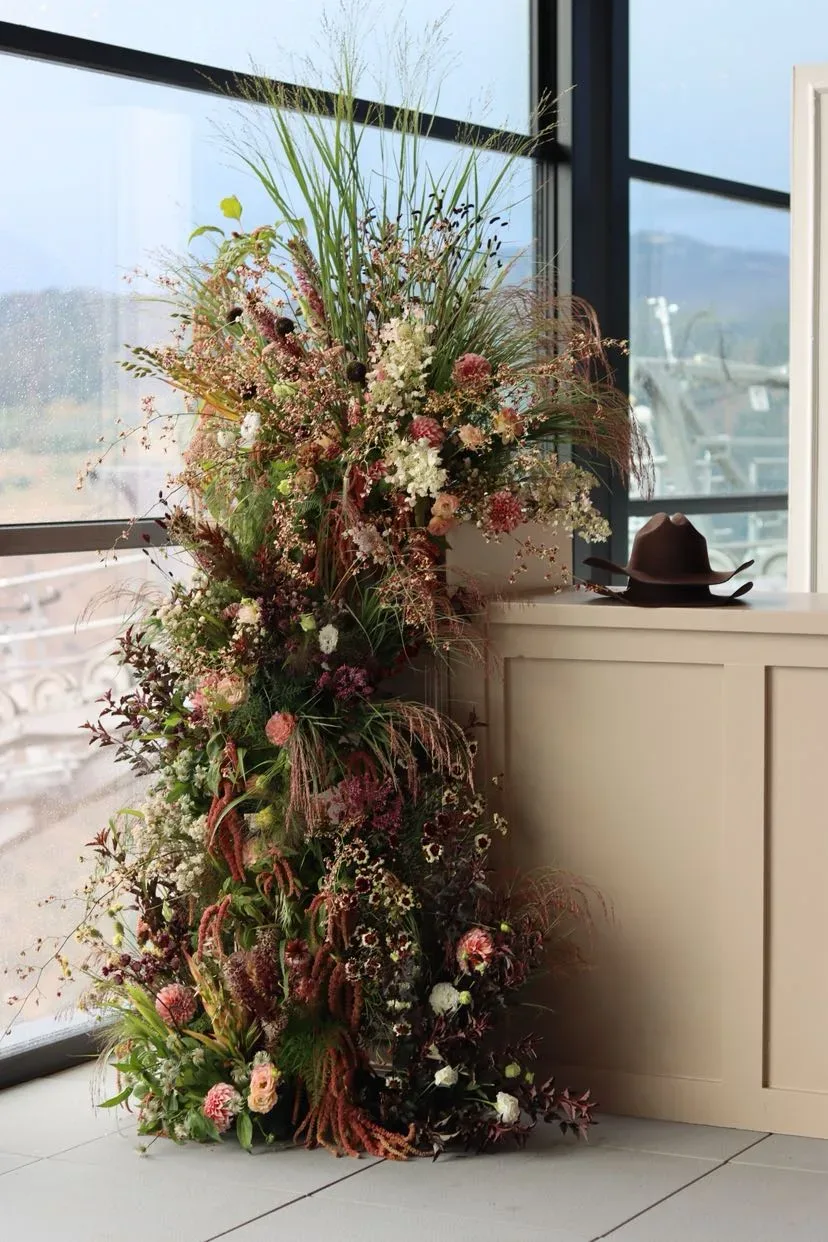 Tall indoor floral column beside a cowboy hat and a window looking toward the mountains
