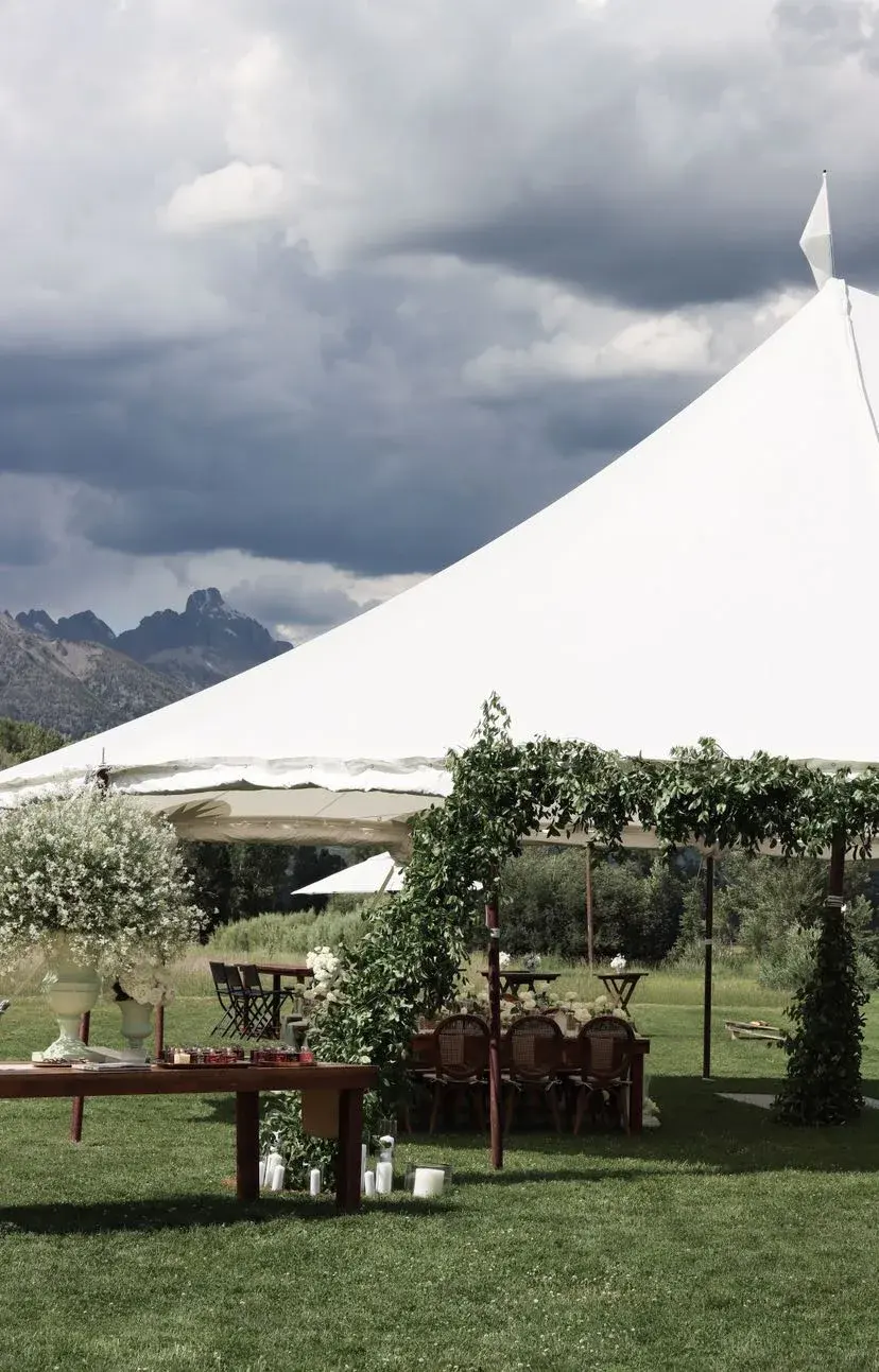 White peaked reception tent with a baby’s breath urn and the Tetons beyond the lawn