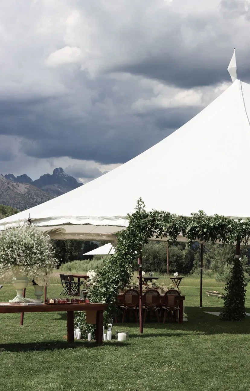 White peaked reception tent with a baby’s breath urn and the Tetons beyond the lawn